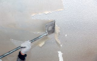 Painter applying white paint to patched drywall cracks section with putty knife in residential interior.