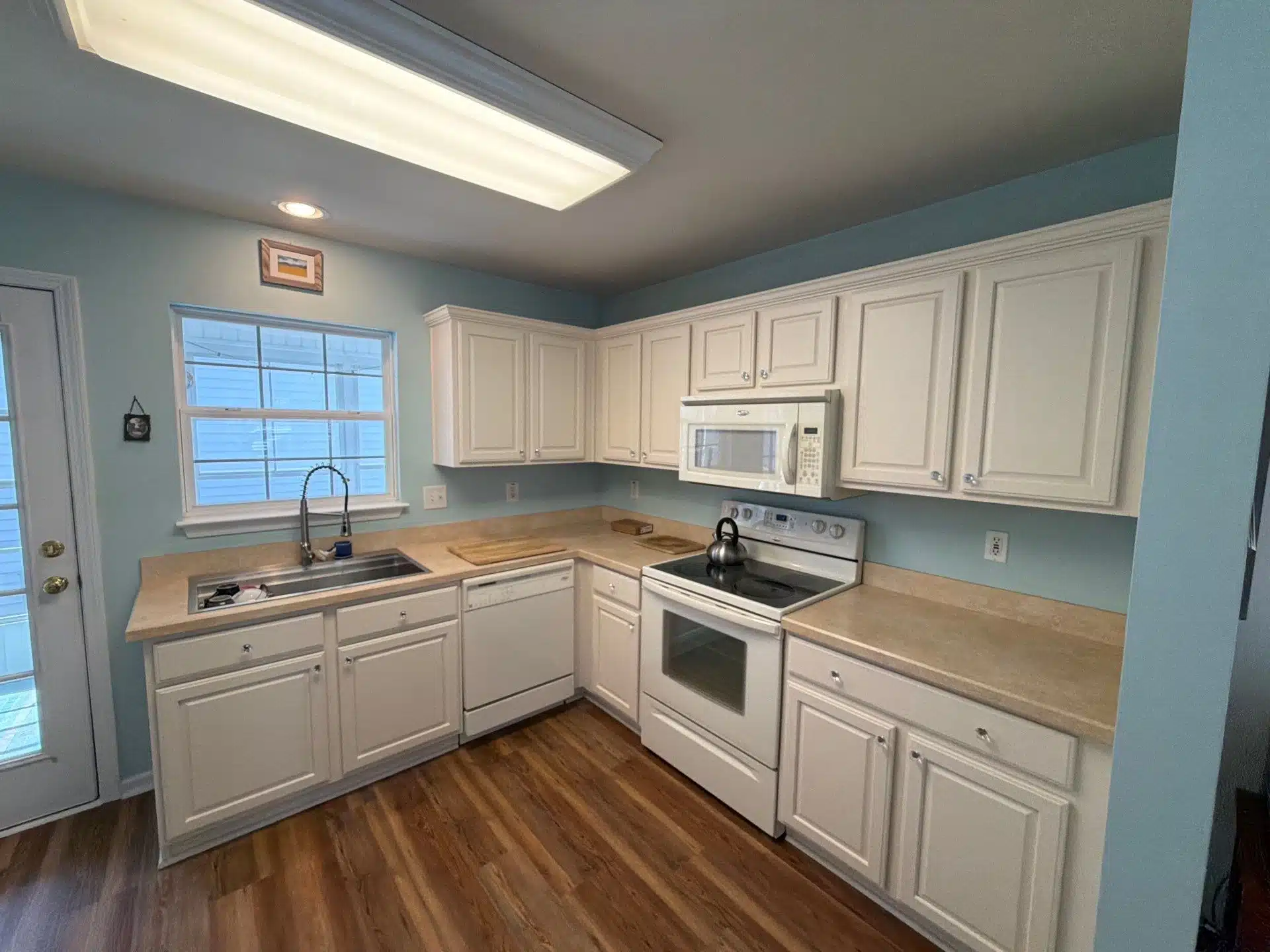 Outdated Kitchen Cream Cabinets Before Painting Service An outdated kitchen featuring cream colored cabinets, light blue walls, and old appliances before professional painting.