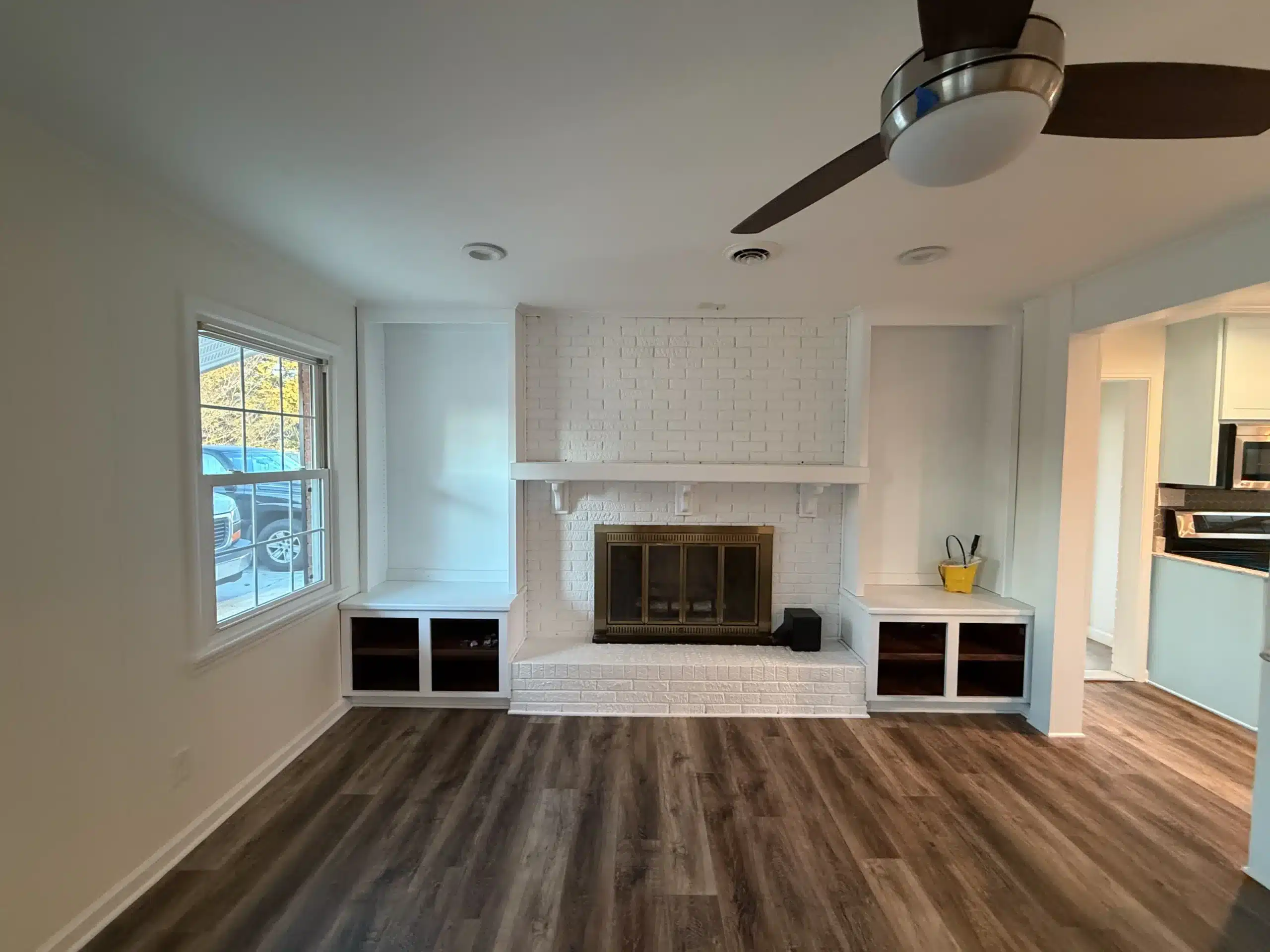White Painted Brick Fireplace with Built In Shelves Living room with a freshly painted white brick fireplace, built in shelving, and a view into the kitchen.