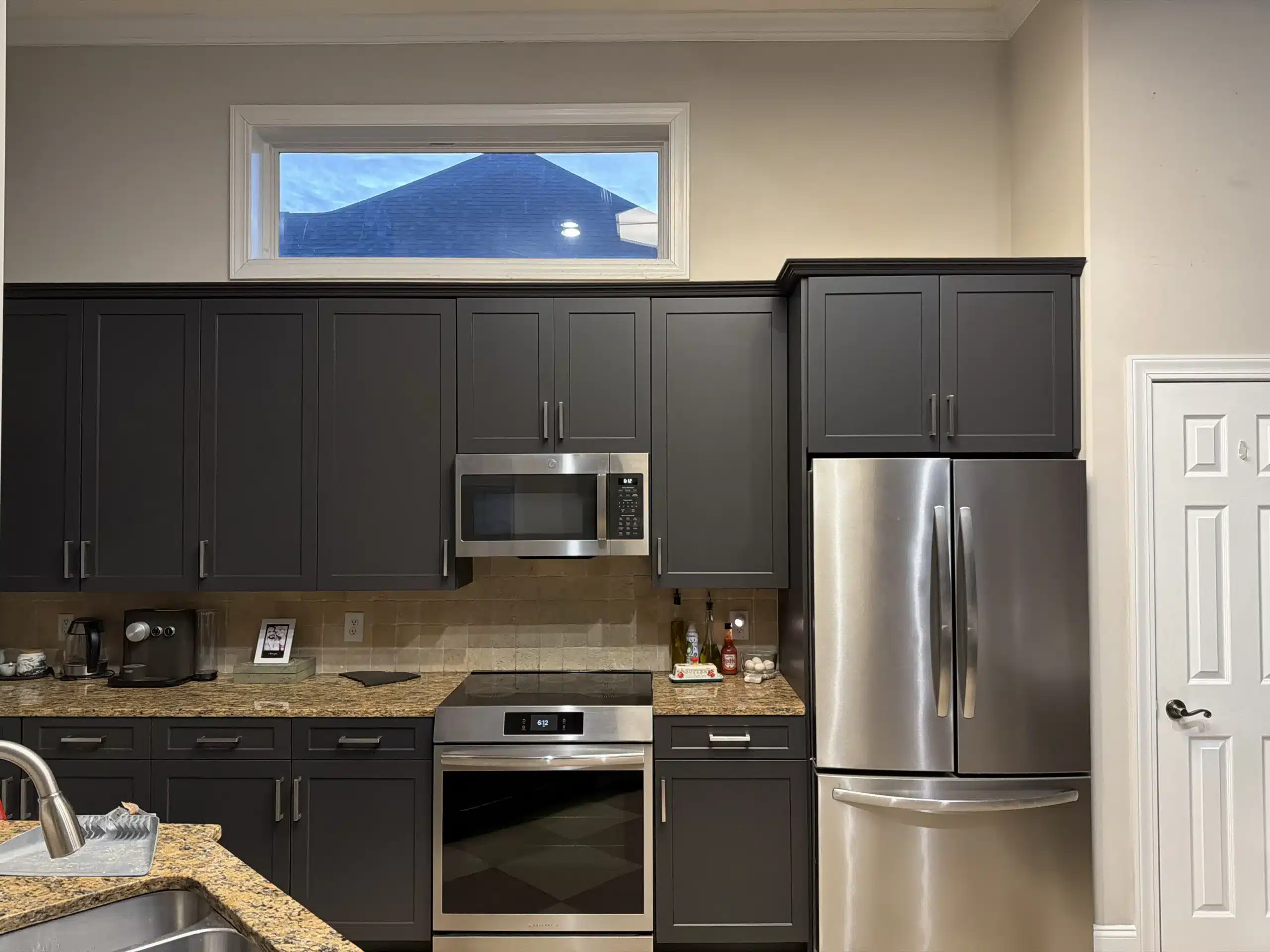 Modern Kitchen with Dark Gray Painted Cabinets and Stainless Steel Appliances Contemporary kitchen showcasing dark gray painted cabinets, sleek stainless steel appliances, and a light tiled backsplash.