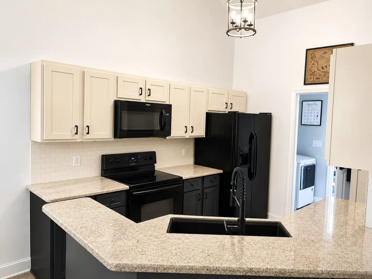 Cream Kitchen Cabinets Black Appliances Cream-painted kitchen cabinets with recessed panel doors and black hardware above black appliances and speckled beige quartz