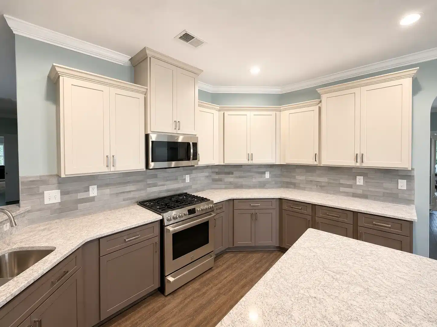 Two Tone Kitchen Cabinets Cream and taupe painted kitchen cabinets with recessed panel doors, brushed nickel hardware, gray tile backsplash, and light