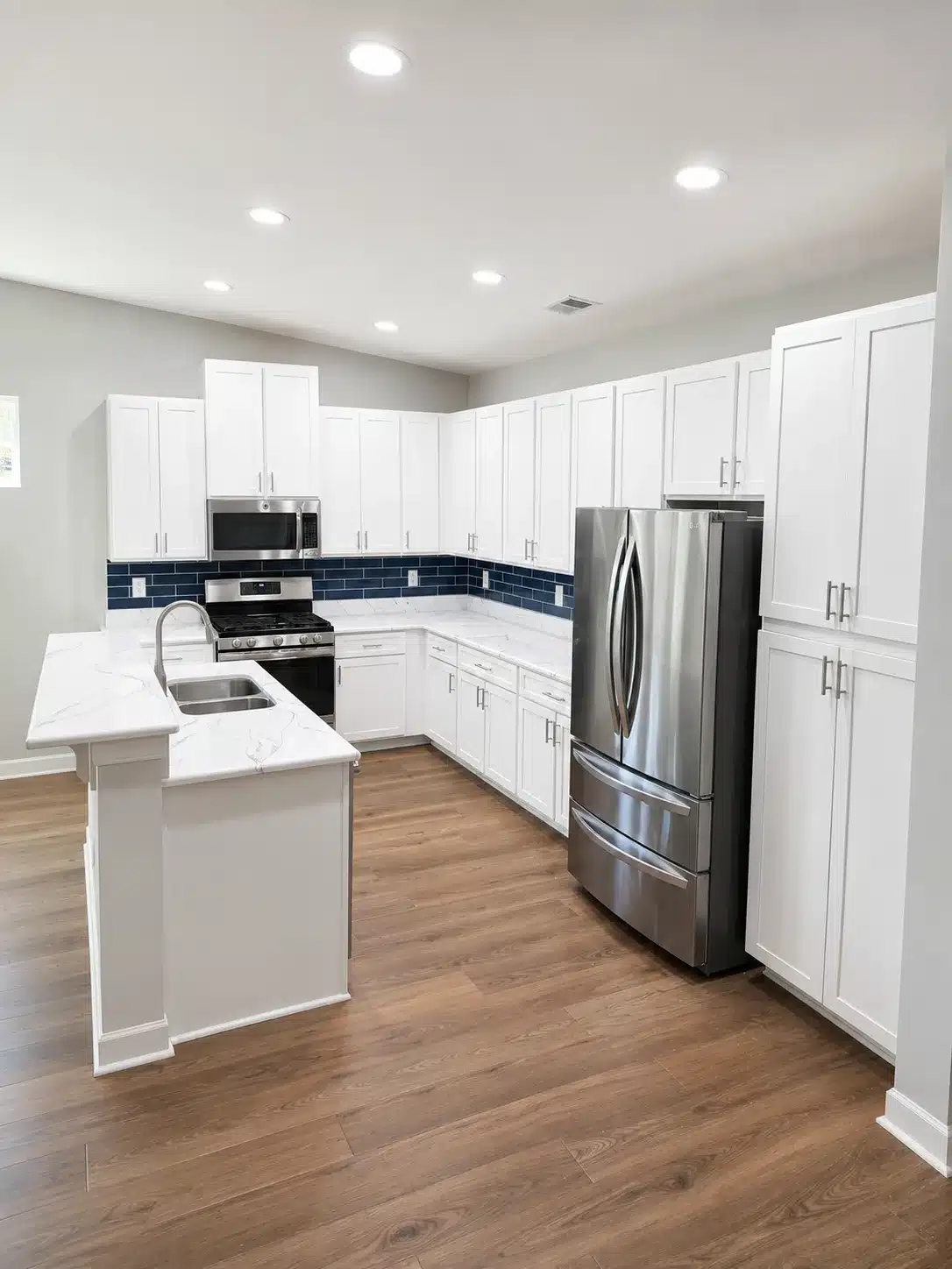 White Painted Kitchen Cabinets White painted kitchen cabinets with recessed panel doors, chrome hardware, white quartz countertop, and navy subway tile