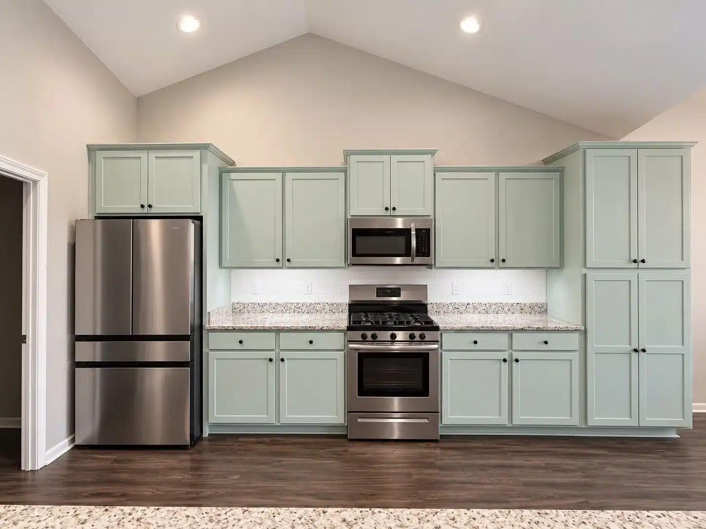 Sage Green Kitchen Cabinetry Sage green-painted kitchen cabinetry with speckled granite countertops, stainless steel appliances, and white subway tile