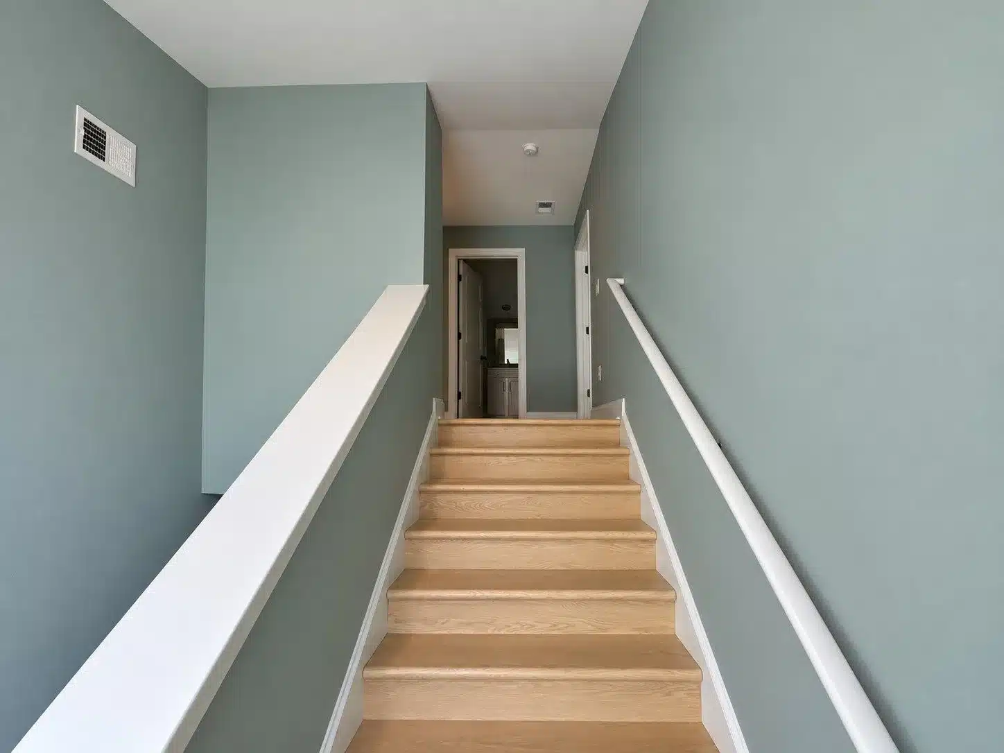 Sage Green Stairwell Hallway Sage green-painted stairwell walls with white ceiling, trim, white railings, and natural wood stairs in residential interior.
