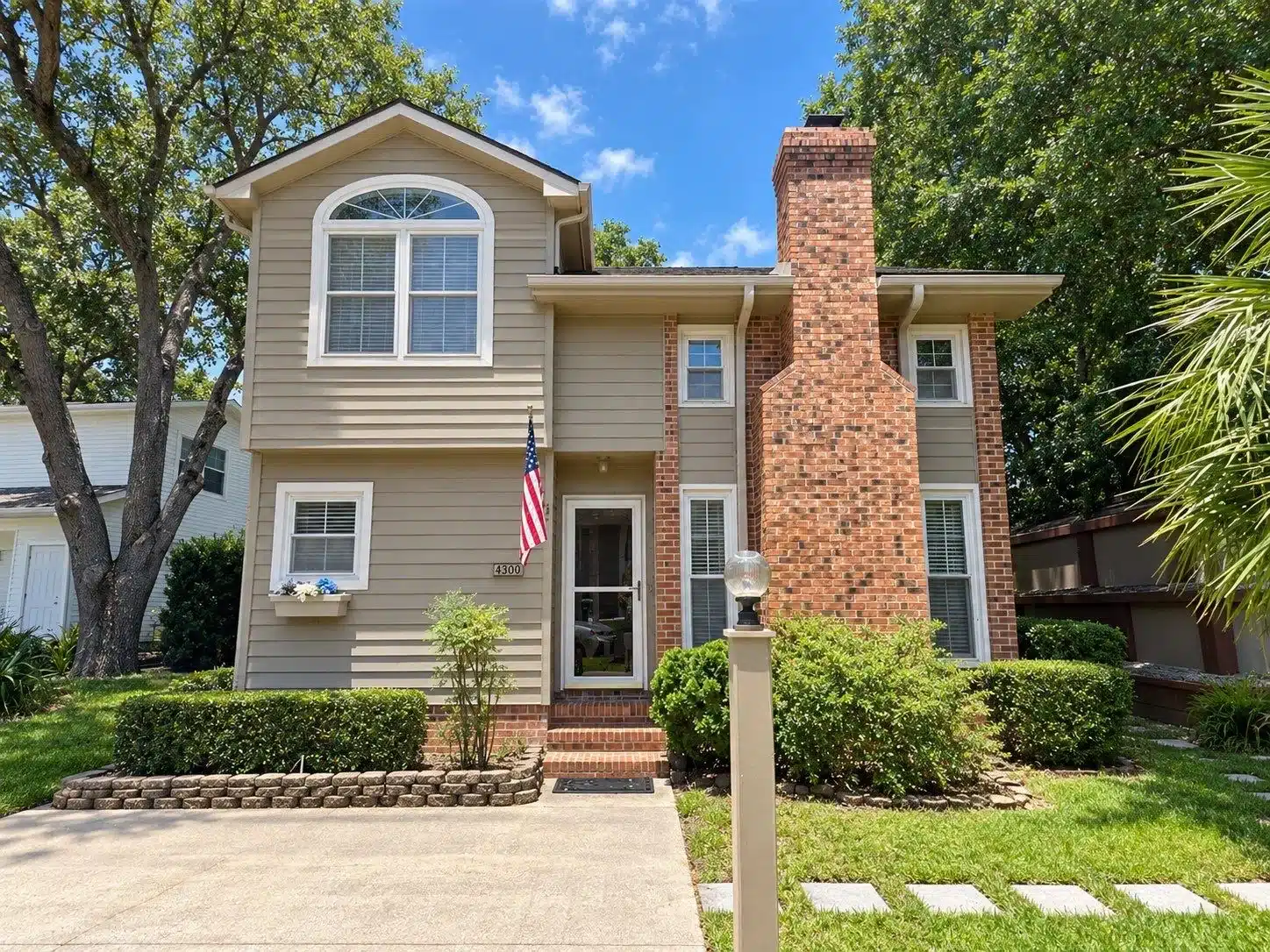 Tan Siding Brick Exterior Home Tan vinyl-sided two-story residential home with red brick chimney, white trim, and arched window in North Myrtle Beach.